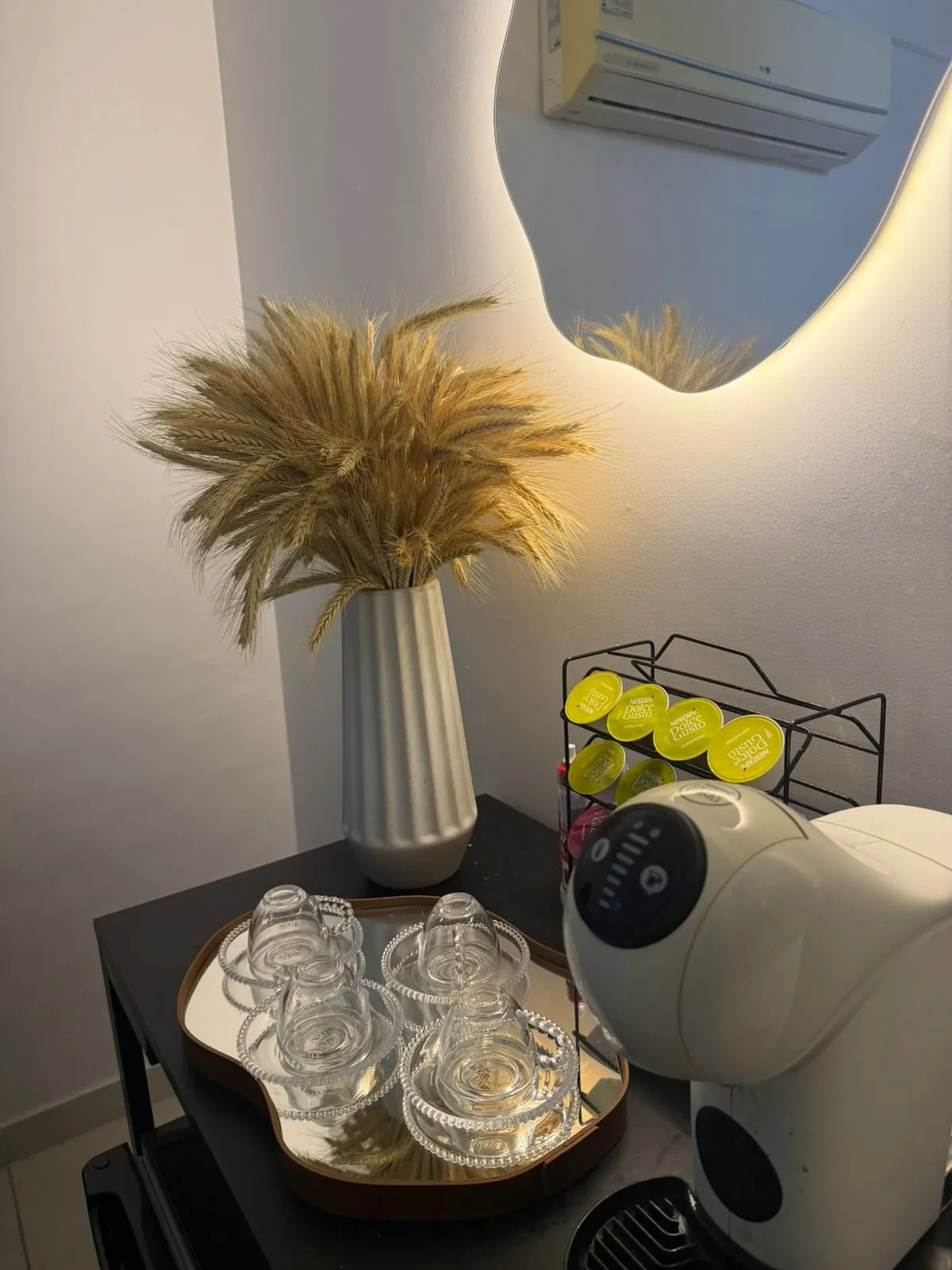 Cantinho do café na recepção: vaso de flores secas, espelho iluminado e cafeteira